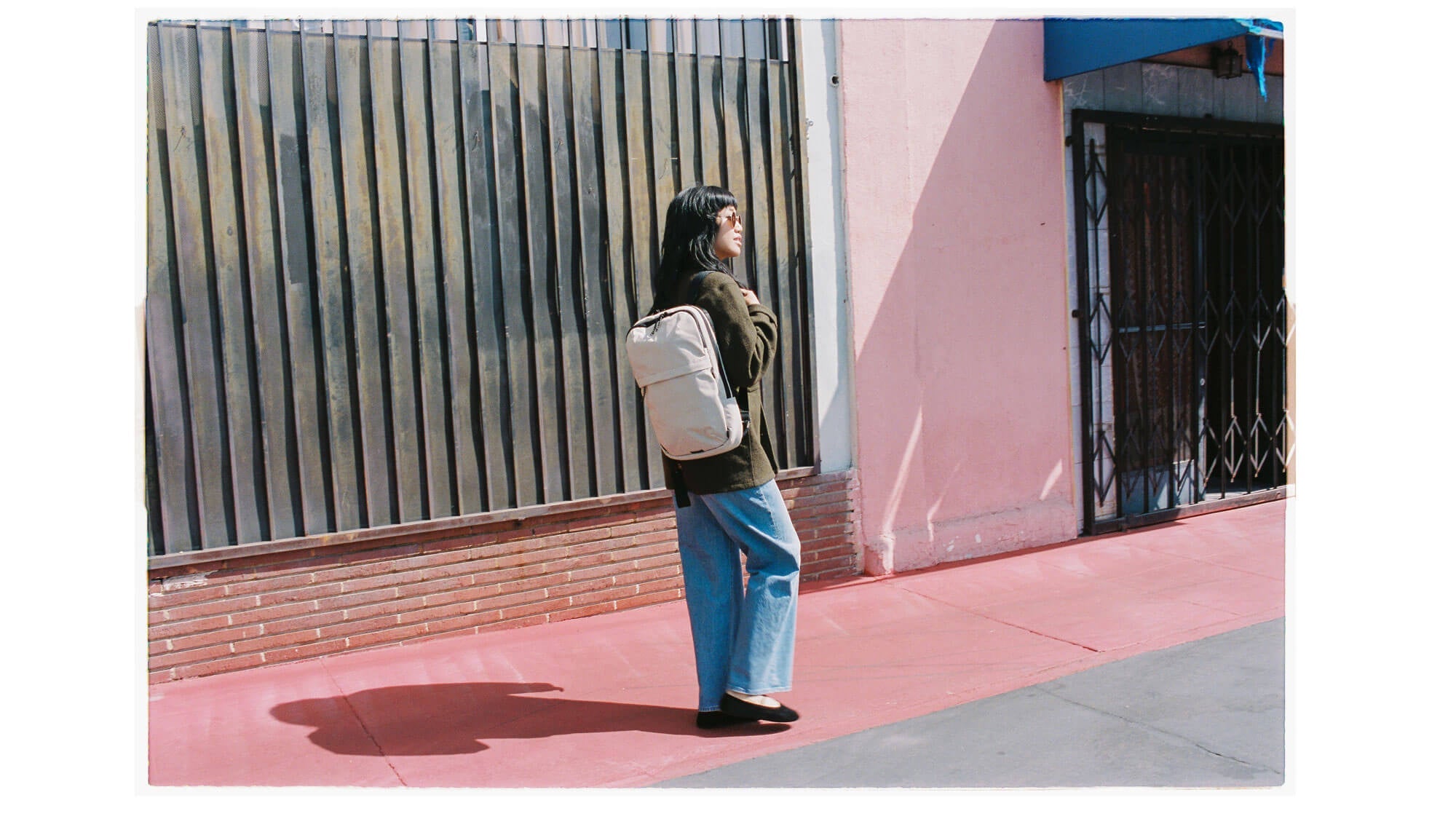 Woman walking in front of a pink wall with the Pakt 15L Bag