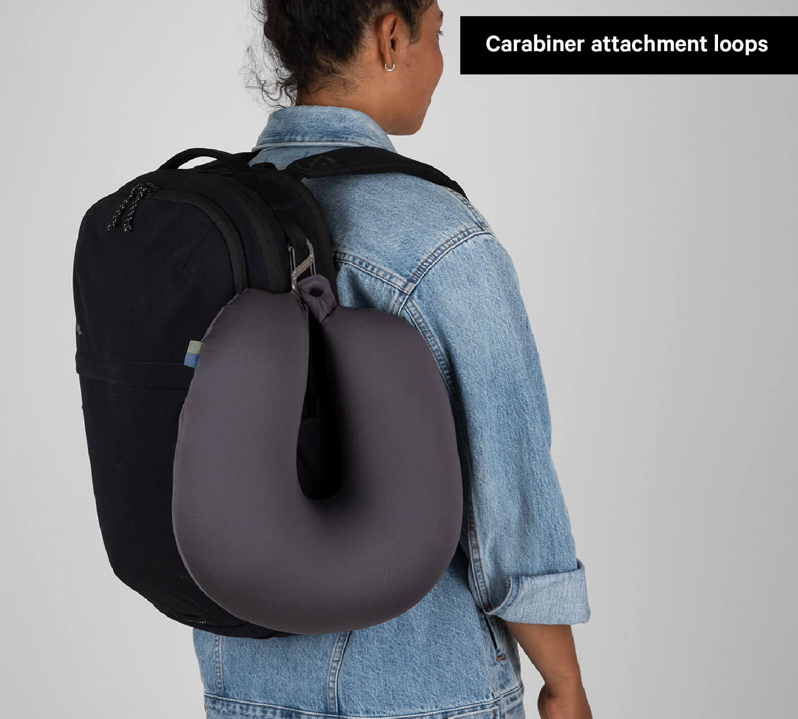 Person wearing Everyday 22L backpack with a travel neck pillow clipped to Carabiner attachment loops.