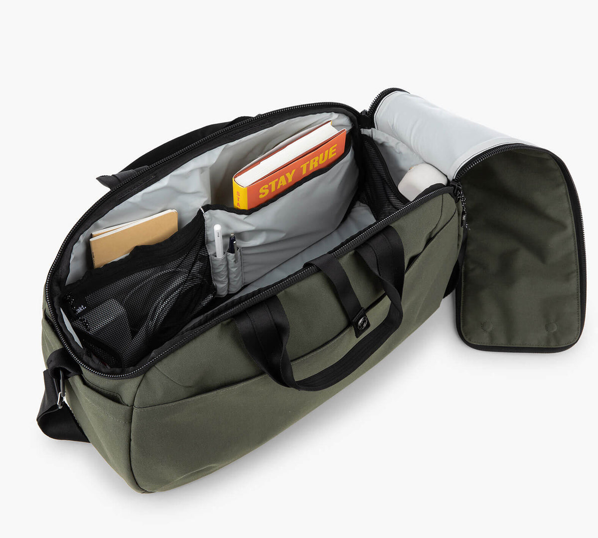 The opening of the 25L Travel Duffel in Forest, showing organized interior compartments with a book titled 'STAY TRUE', pens, and other items inside.