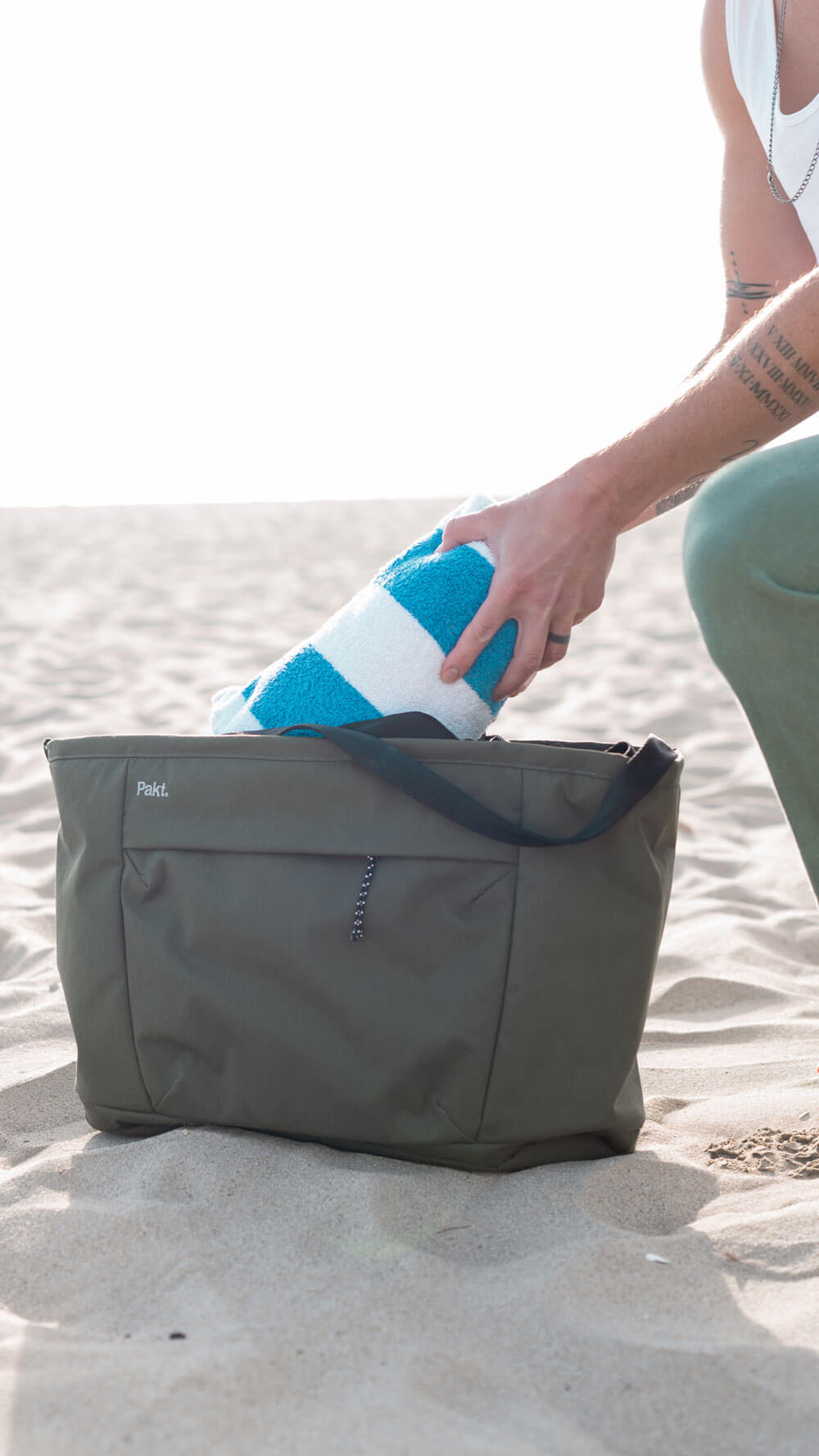 Front view of Everyday 25L Tote in cypress showcasing exterior front pocket and shoulder straps on a sandy beach