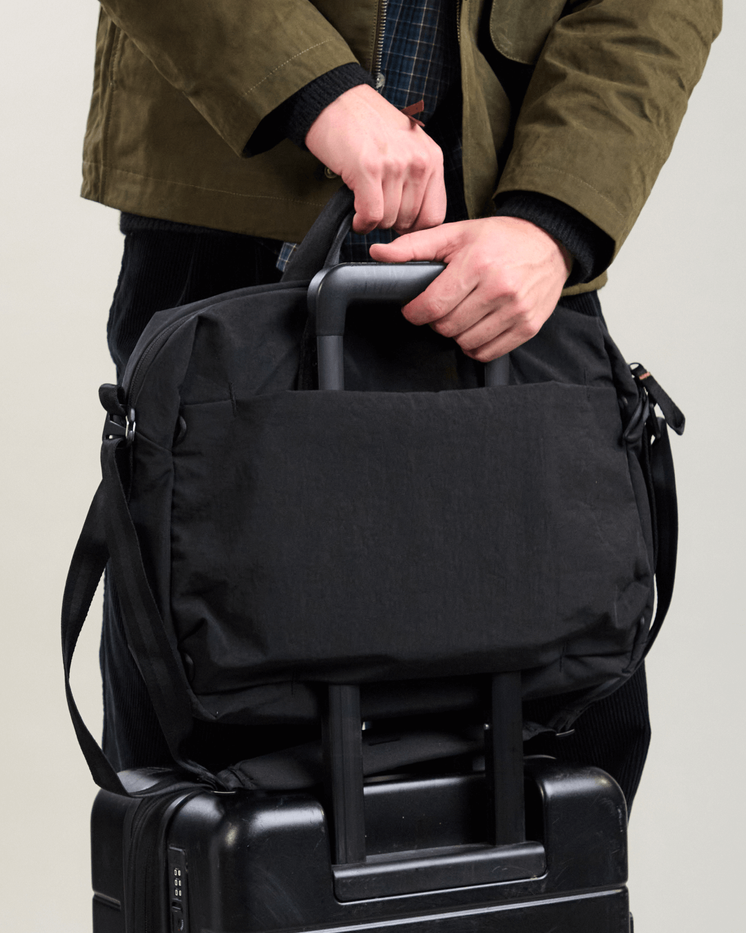 Front view of MODE Shoulder Bag 12L showing luggage pass through sleeve secured over a rolling suitcase handle with hands