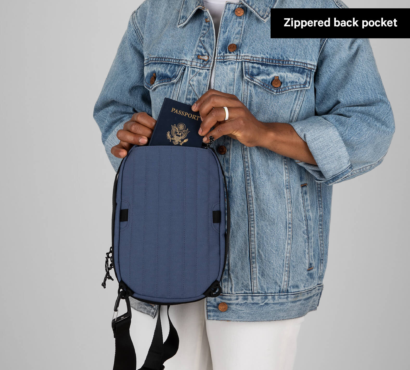 Person holding a blue Everyday 5L Sling bag with a passport partially inside the zippered back pocket labeled 'Zippered back pocket'
