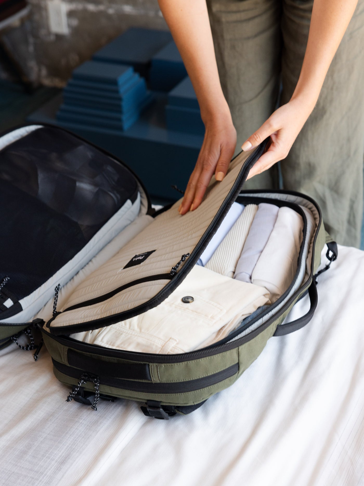 Person packing a green suitcase with neatly folded clothes on a bed.