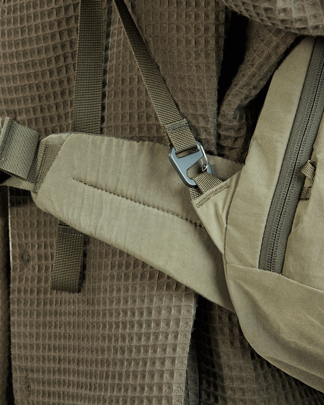 Close-up of Pakt One Travel Backpack hip belt in cypress showing padded strap, quick-release buckle, and adjacent zip pocket