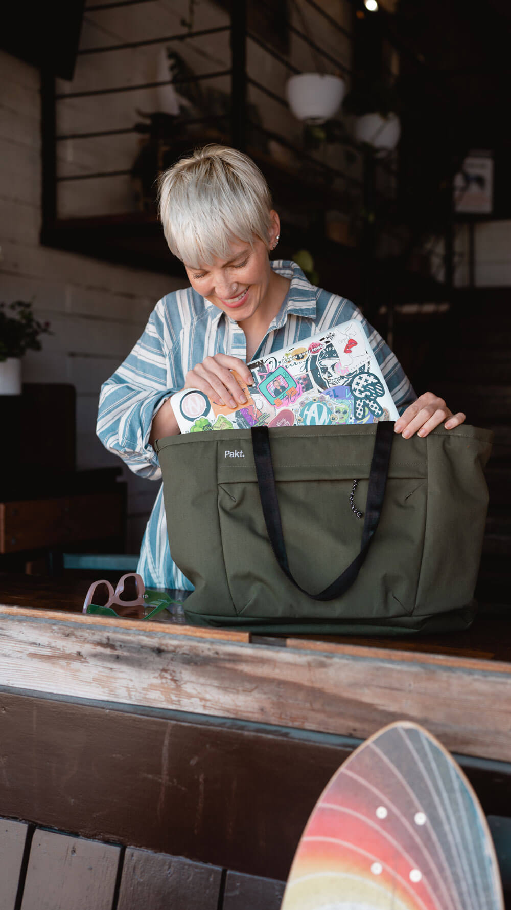 Three-quarter view of Everyday 25L Tote in cypress with roomy main compartment as a person places a laptop