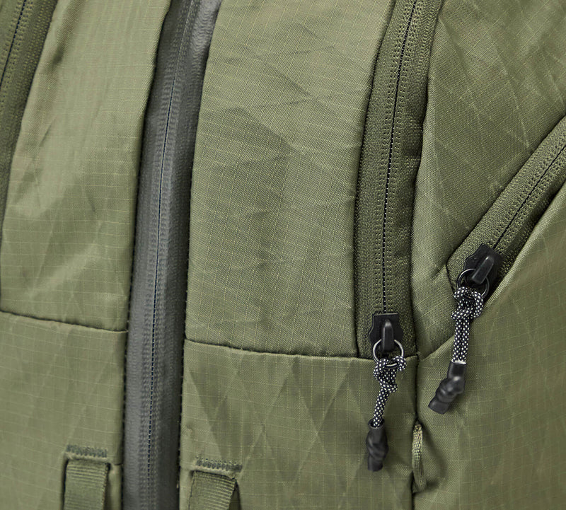 Close-up of the Cypress Aero Travel Backpack showing the fabric with two black zipper pulls on a travel bag or backpack.