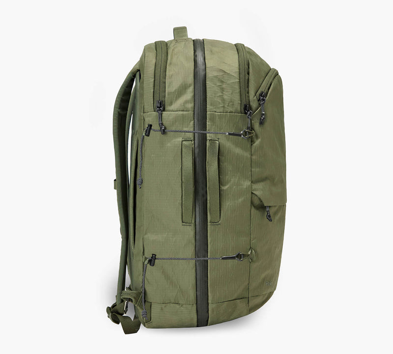 Olive-green travel backpack, side profile showing vertical front zip, shoulder straps, and side pocket.