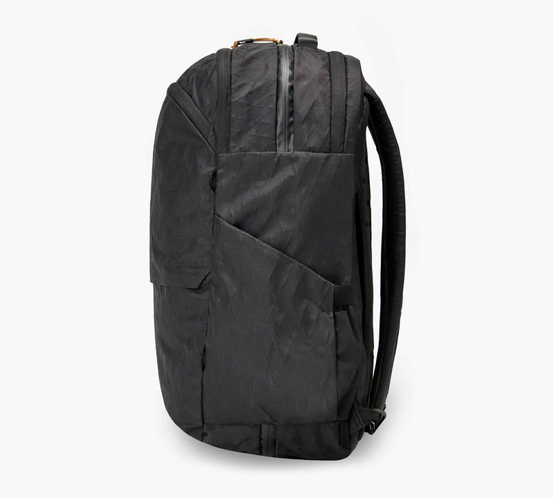 Black padded backpack seen from the side, with padded shoulder straps, side pocket, and top carry handle.