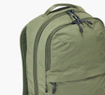 Olive green backpack with two zippered compartments, top carry handle, and shoulder strap, front-side close-up.