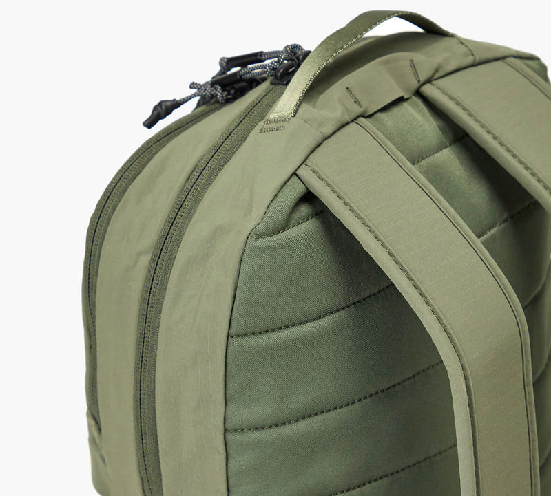 Olive-green backpack back panel showing padded shoulder straps, top handle, and zipper pull