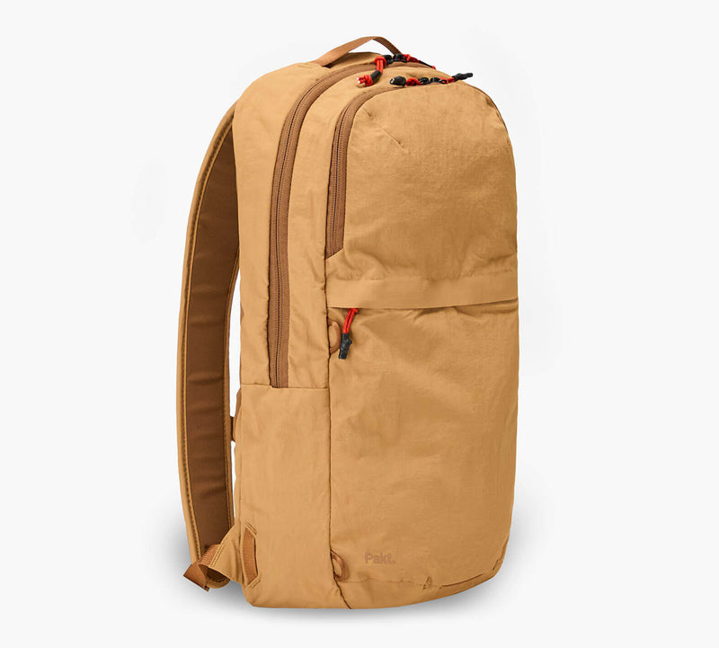 Tan packable 16L backpack, side view with red zipper pulls and Pakt. logo