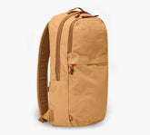 Mojave tan backpack, side view of a slim two-compartment canvas daypack with top handle and zip pockets.