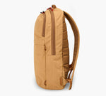 Tan padded backpack, side profile showing two zippered compartments, slim side pocket and padded shoulder straps.
