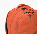 Orange backpack with front zip pocket and red-black zipper pulls, top carry handle