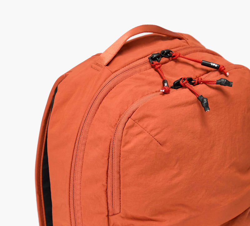 Orange backpack with front zip pocket and red-black zipper pulls, top carry handle