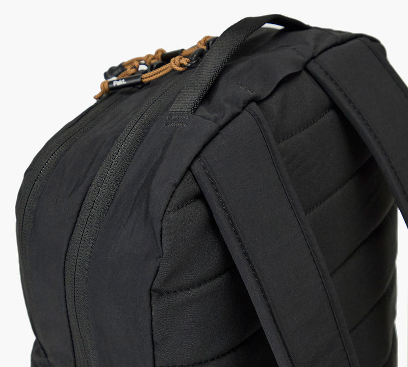 Close-up of black backpack top corner showing padded shoulder strap, zippered compartment, and leather zipper pulls.