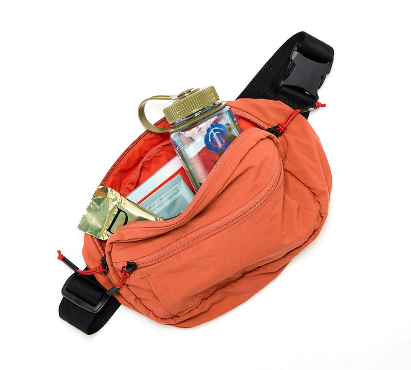 Open orange waist pack showing clear water bottle, folded map, and crumpled cash inside.