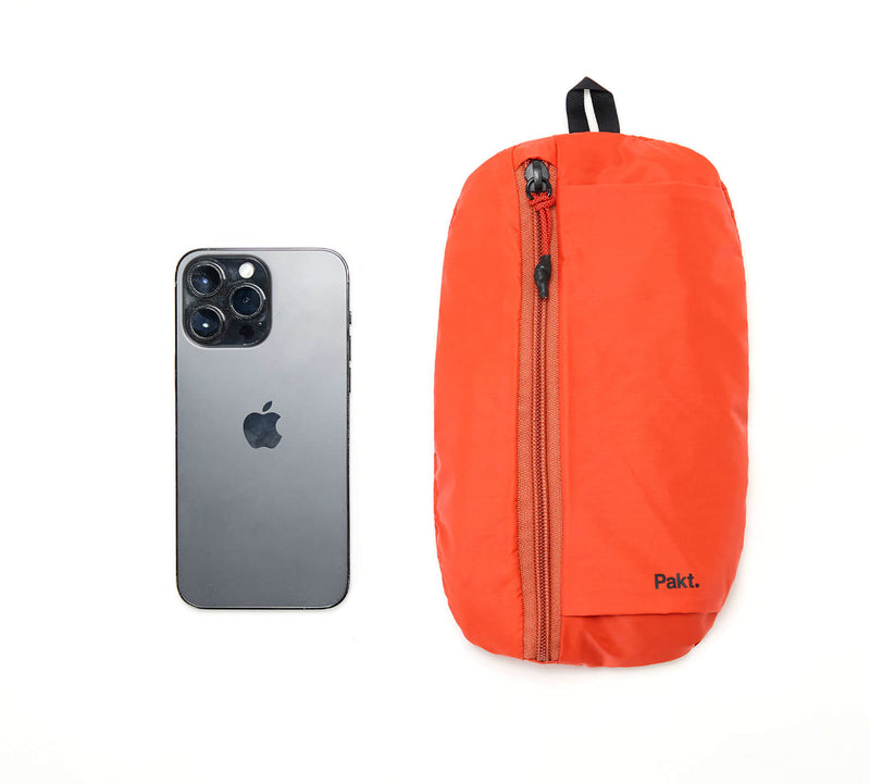 Orange Stash Packable Sling 4L bag next to a black smartphone on white background