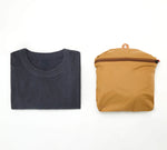 Folded dark gray t-shirt next to a mustard yellow Stash Packable Tote 20L packed flat - showing the comparison 