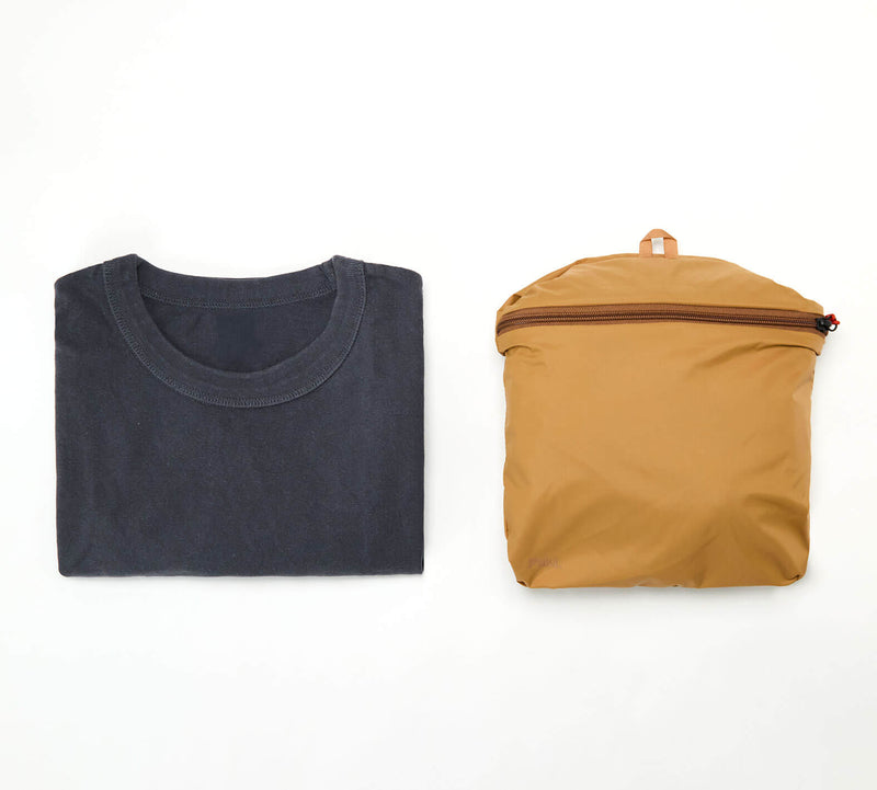 Folded dark gray t-shirt next to a mustard yellow Stash Packable Tote 20L packed flat - showing the comparison 