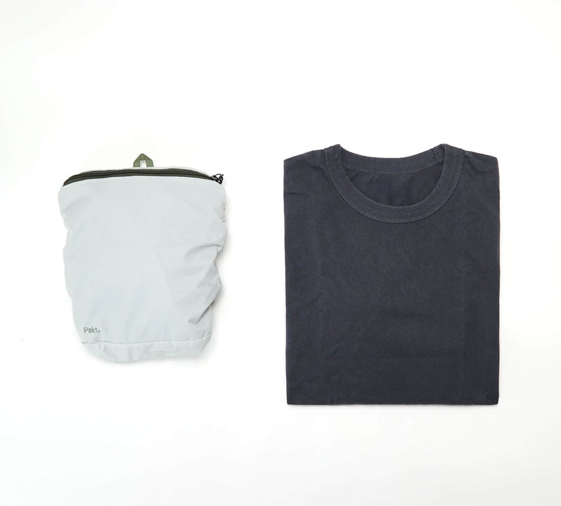Folded light gray packable backpack next to a folded dark gray shirt on white background