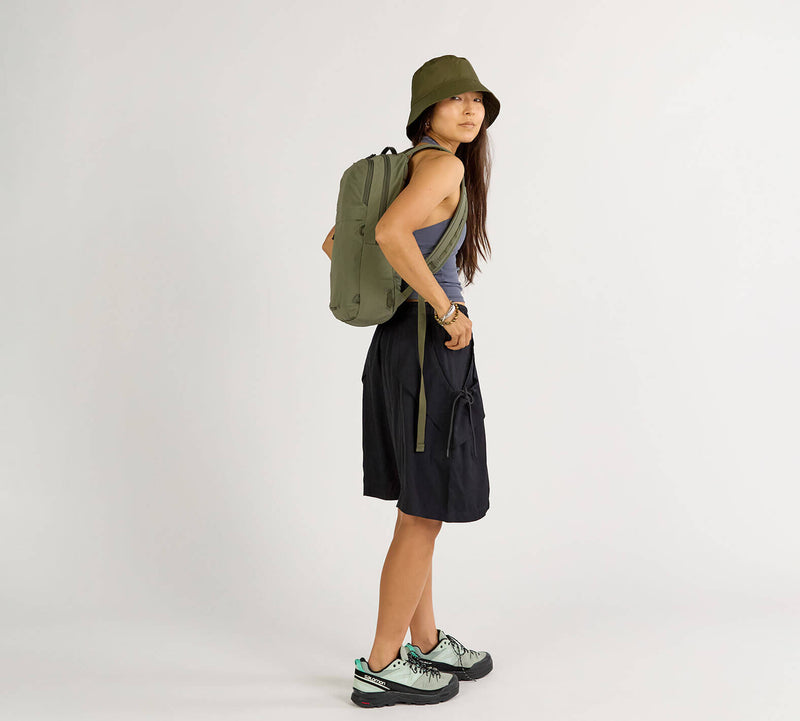 Woman wearing Stash Packable Backpack 16L in olive green, standing sideways in casual outfit.