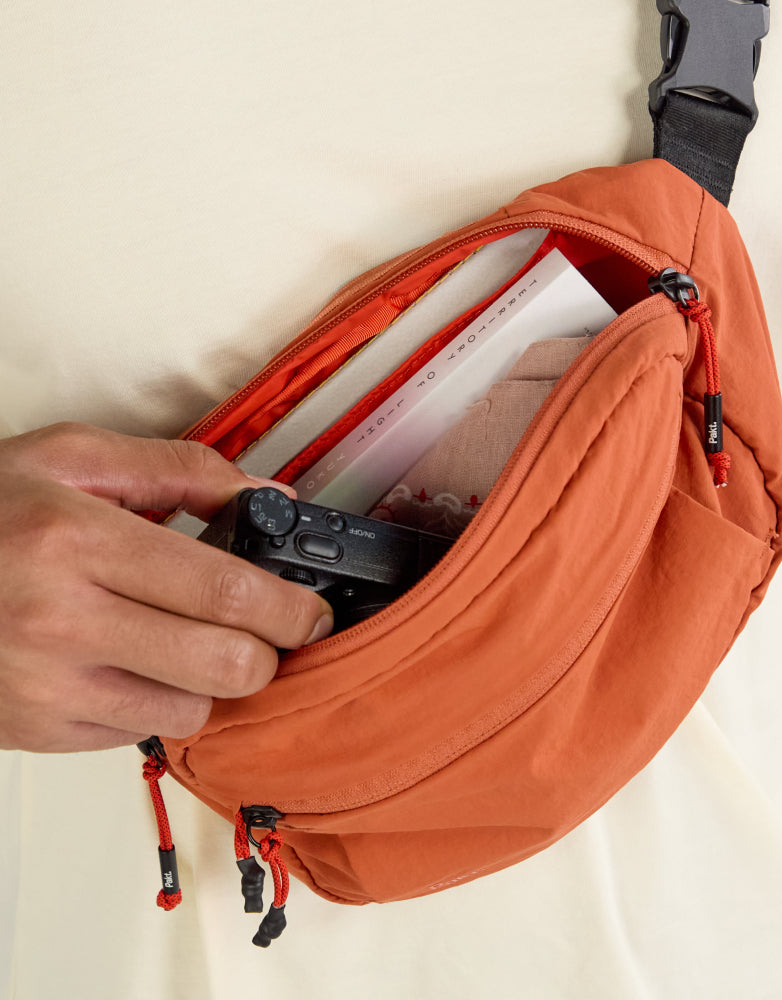 Top view of Stash Packable Sling 4L in sumac showing open main compartment with camera and inner slip pocket worn cross-body