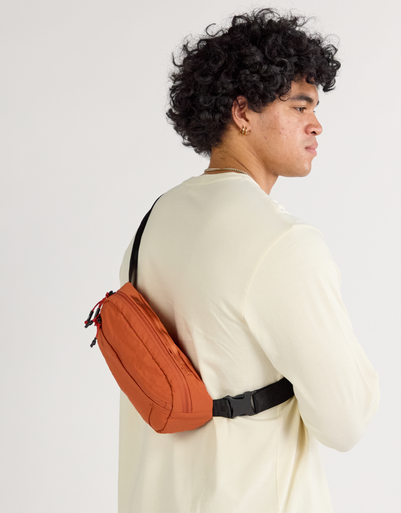 Model wearing sumac Stash Packable Sling 4L cross-body over the back with waist buckle, plain light studio background