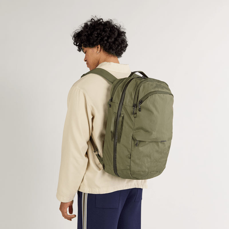 Rear view of Cero Travel Backpack in cypress worn by a model against a light studio background