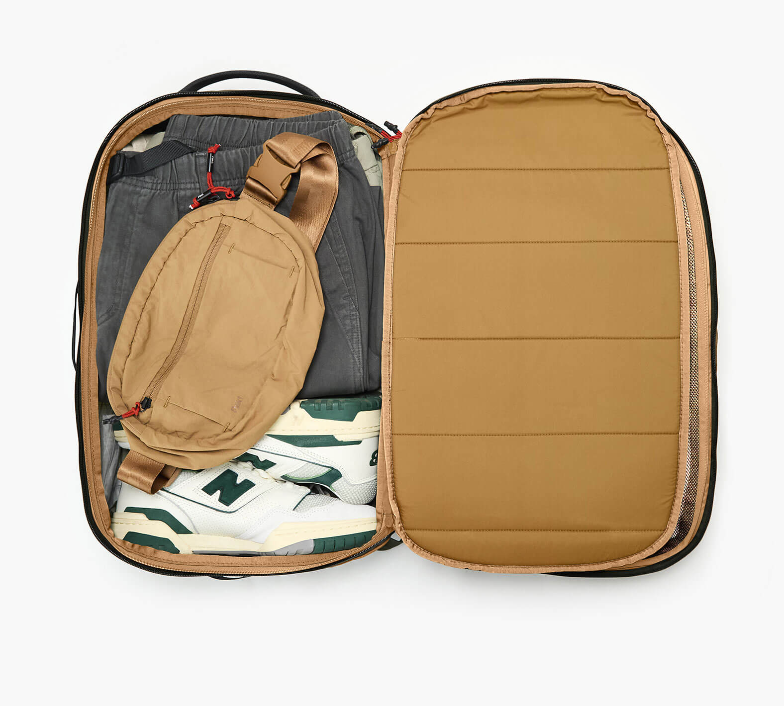 Pakt One Travel Backpack+ open, mojave interior packed with tan sling, gray pants, and white sneakers with green N logo