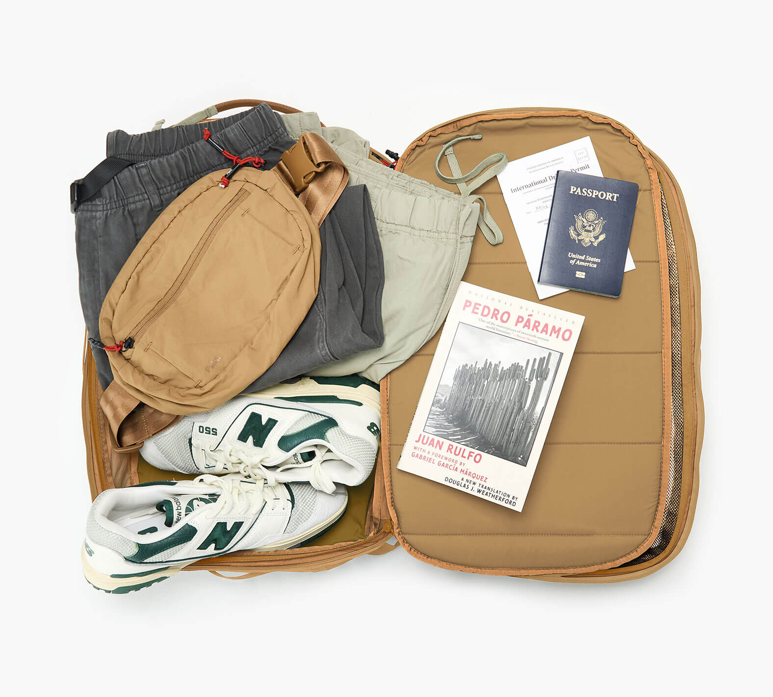 Open Cero Travel Backpack in Mojave showing sneakers, clothes, passport and a paperback on white background