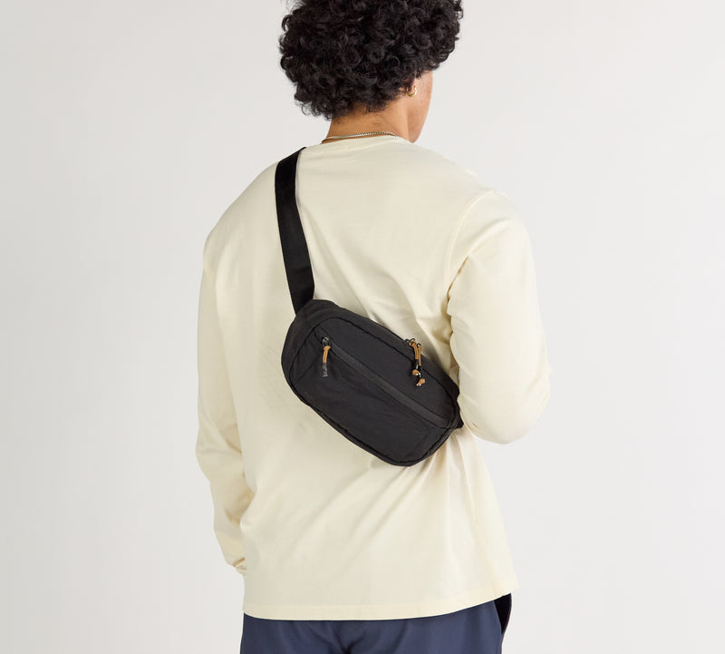 Black Stash Sling crossbody bag worn across the back over a cream long-sleeve shirt