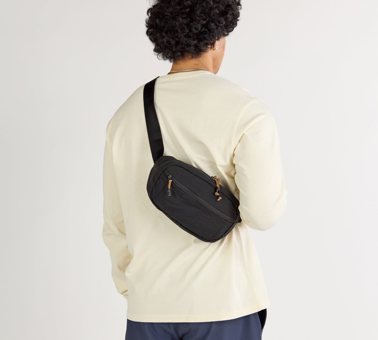 A model wearing a white shirtwith the Stash Sling in Black worn over.