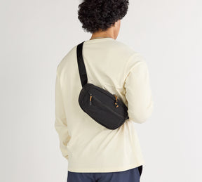 A model wearing a white shirtwith the Stash Sling in Black worn over.