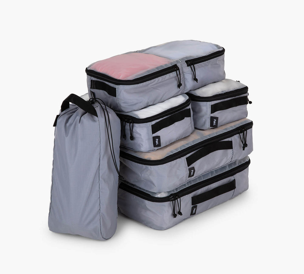 Three-quarter view of a 6-piece packing cube set showing stackable zippered cubes in multiple sizes with a slim carry pouch on a white background