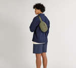 A model wearing a blue shirt with the Stash Sling in Cypress worn over.