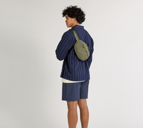 A model wearing a blue shirt with the Stash Sling in Cypress worn over.