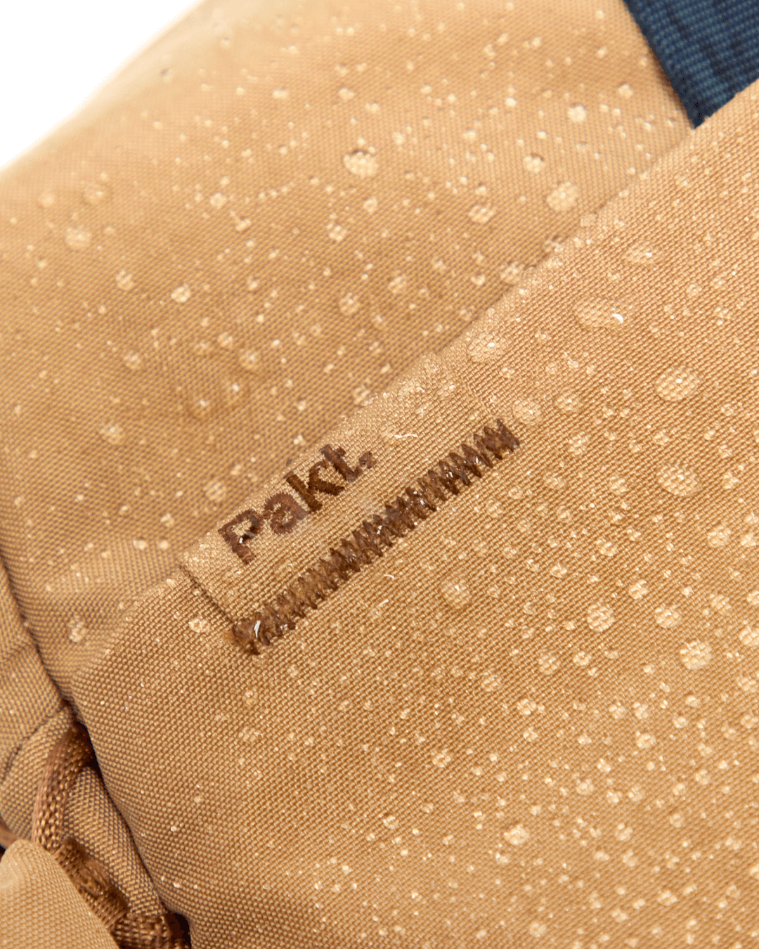 Close-up of MODE Convertible Bag 14L showcasing water beading on mojave fabric with visible stitched Pakt tag