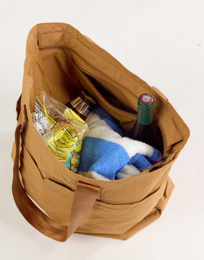Top-down view of Stash Packable Tote 20L in mojave showing interior zippered pocket and packed with towel, wine, and snacks