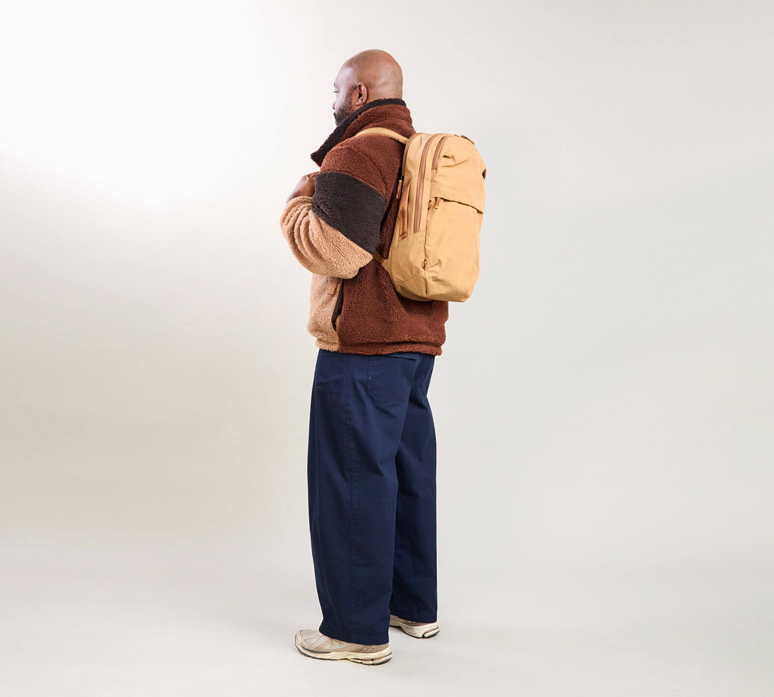 Side view of MODE Backpack 22L in Mojave showcasing side water-bottle pocket, worn on model against pale background