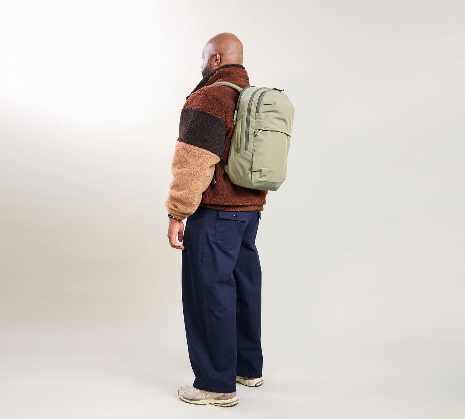 Rear three-quarter view of MODE Backpack 22L in cypress showing side water-bottle pocket, front zip compartments, and padded back against a light studio background