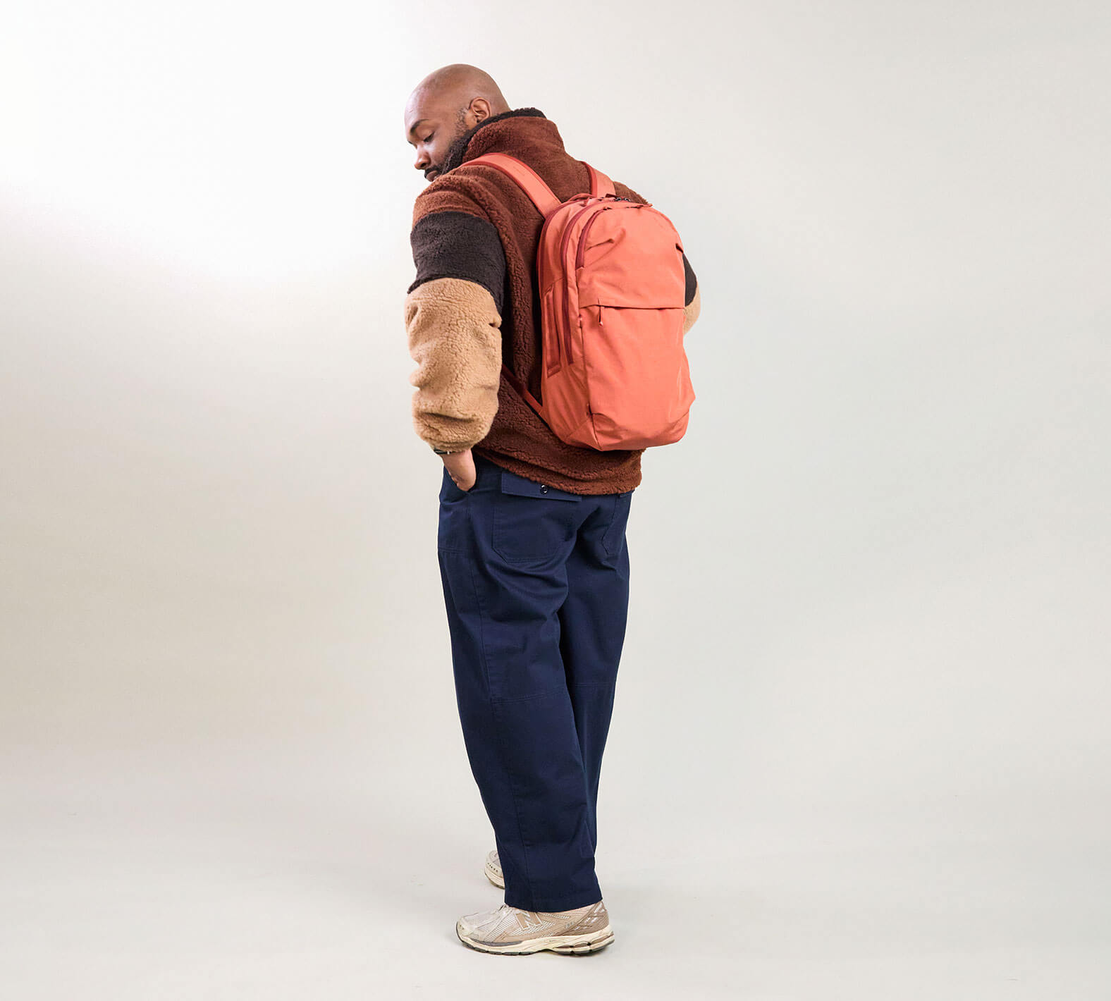Rear three-quarter view of MODE Backpack 22L in Sumac showing padded straps and exterior zip pocket on studio backdrop