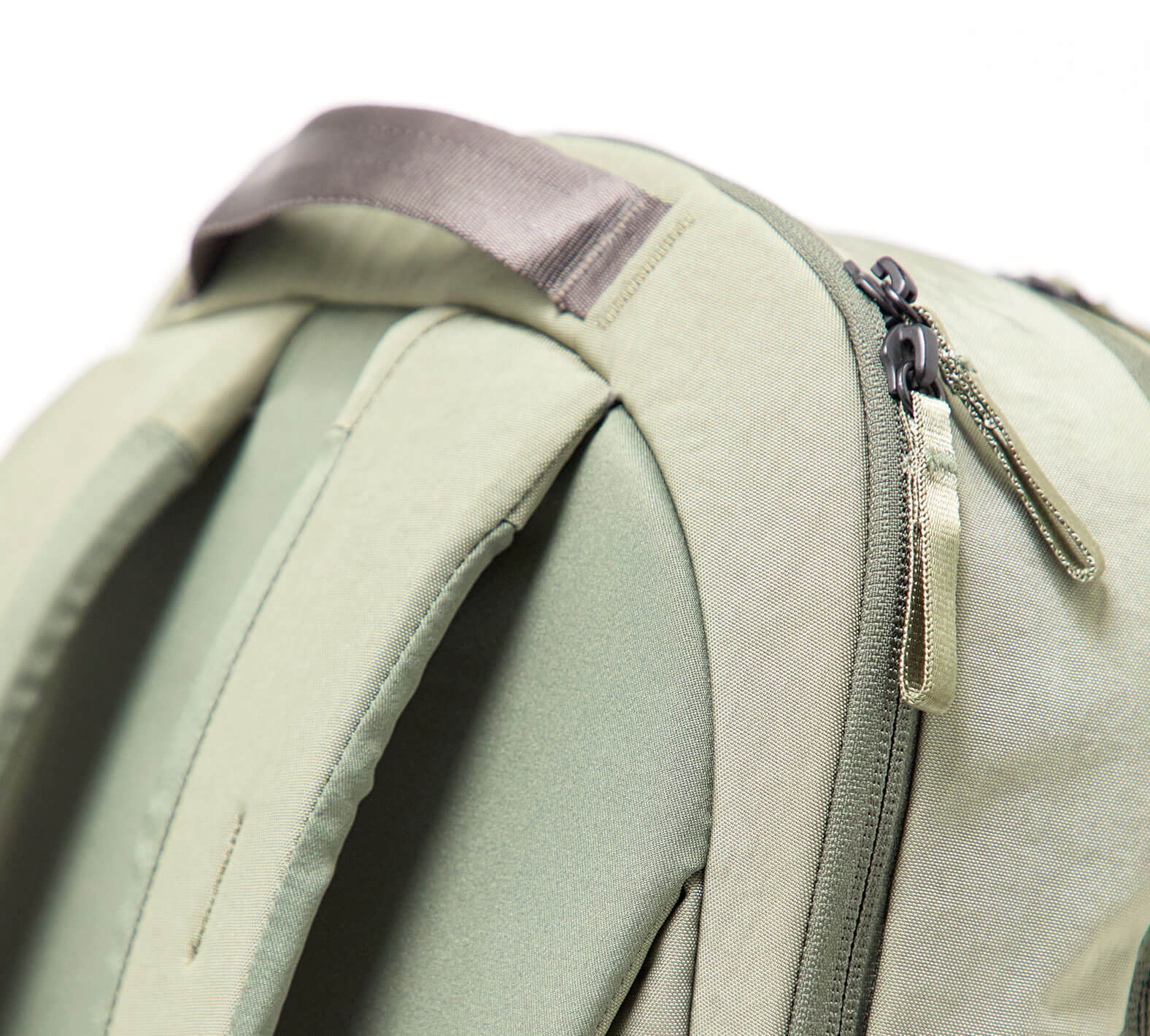 Light olive backpack close-up showing padded shoulder straps, top grab handle, and zipper pulls.