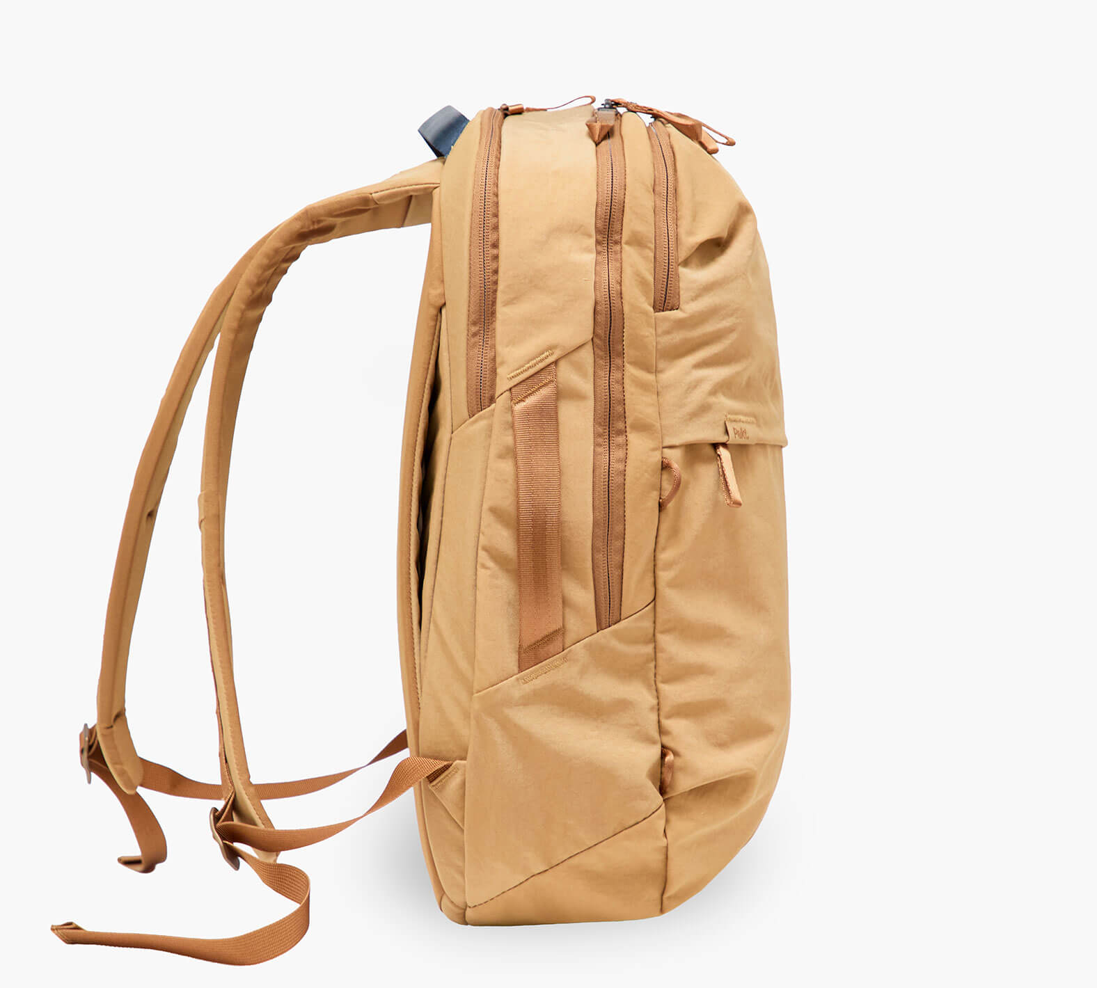 Side profile of tan backpack with padded shoulder straps, top handle, two zippered compartments and a slim side pocket