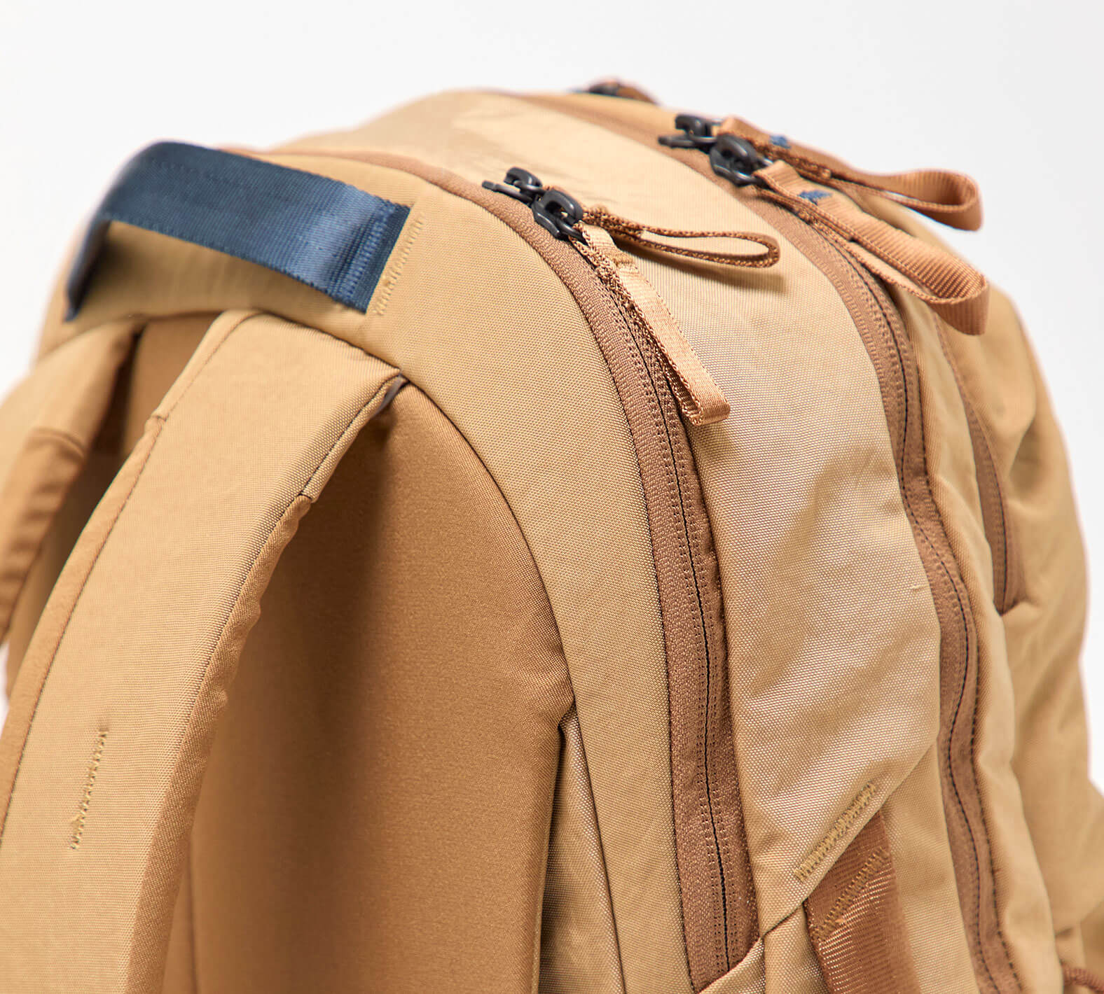 Tan backpack top with padded handle, dual zipper pulls, and front compartment seam