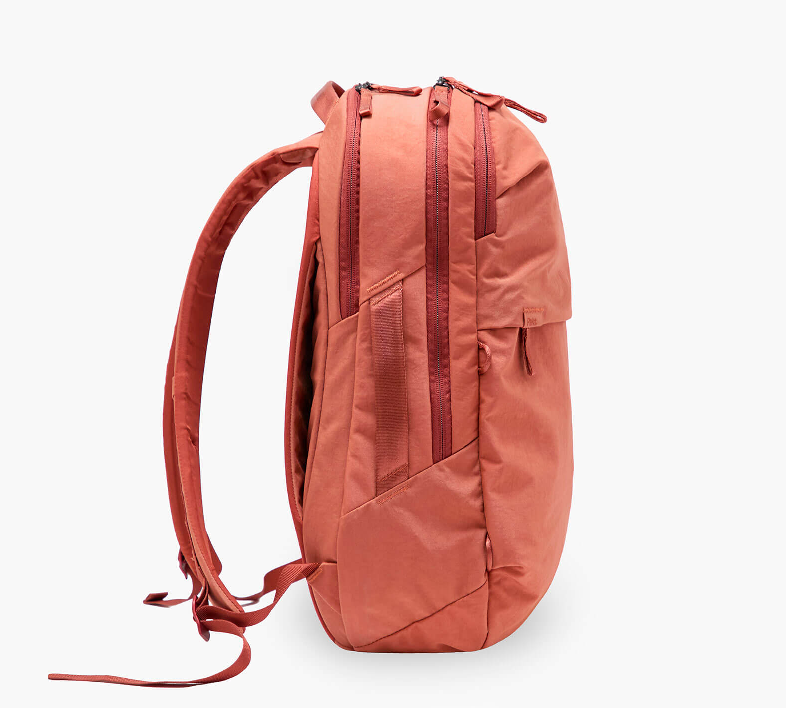 Coral-orange backpack side profile showing two zippered compartments, front pocket, and padded shoulder straps.
