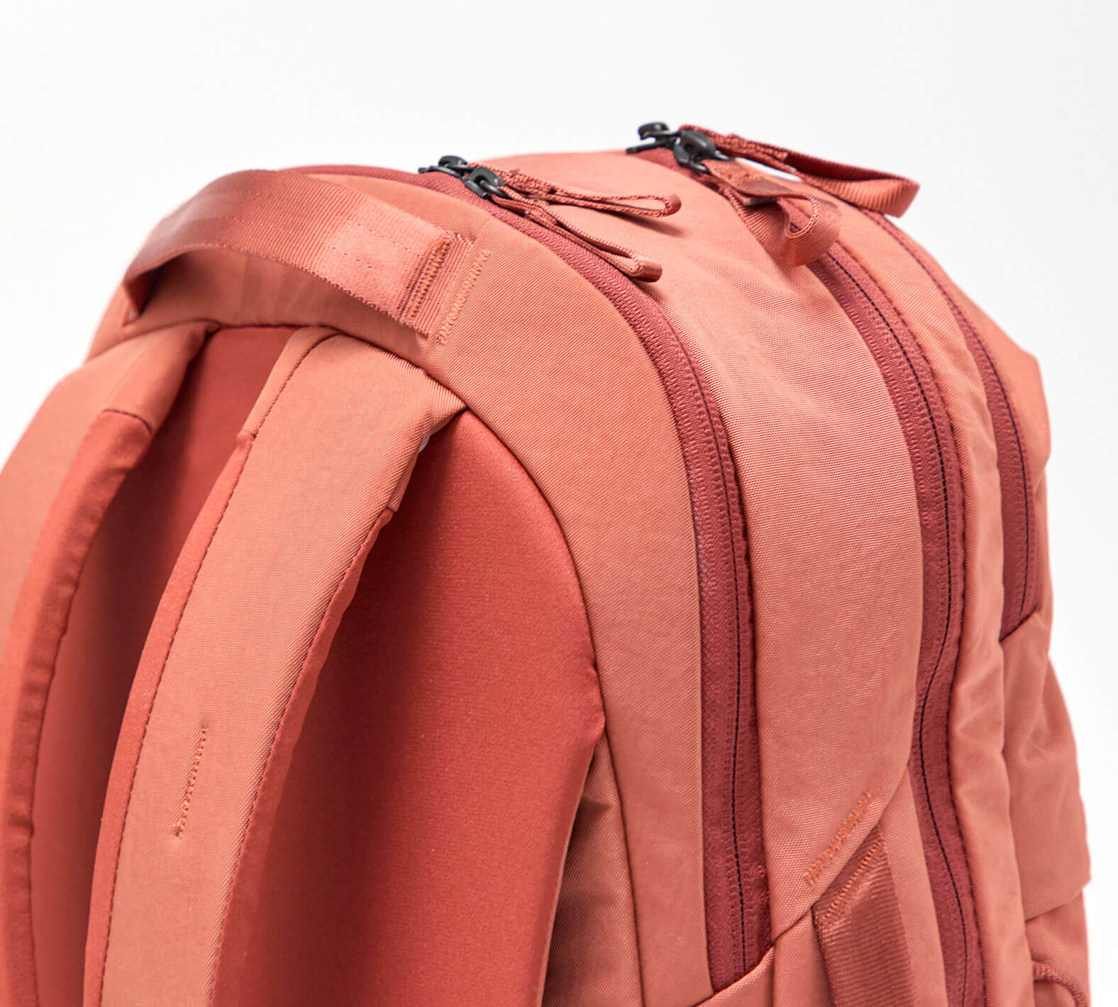 Coral backpack close-up showing padded shoulder straps and two zippered compartments.