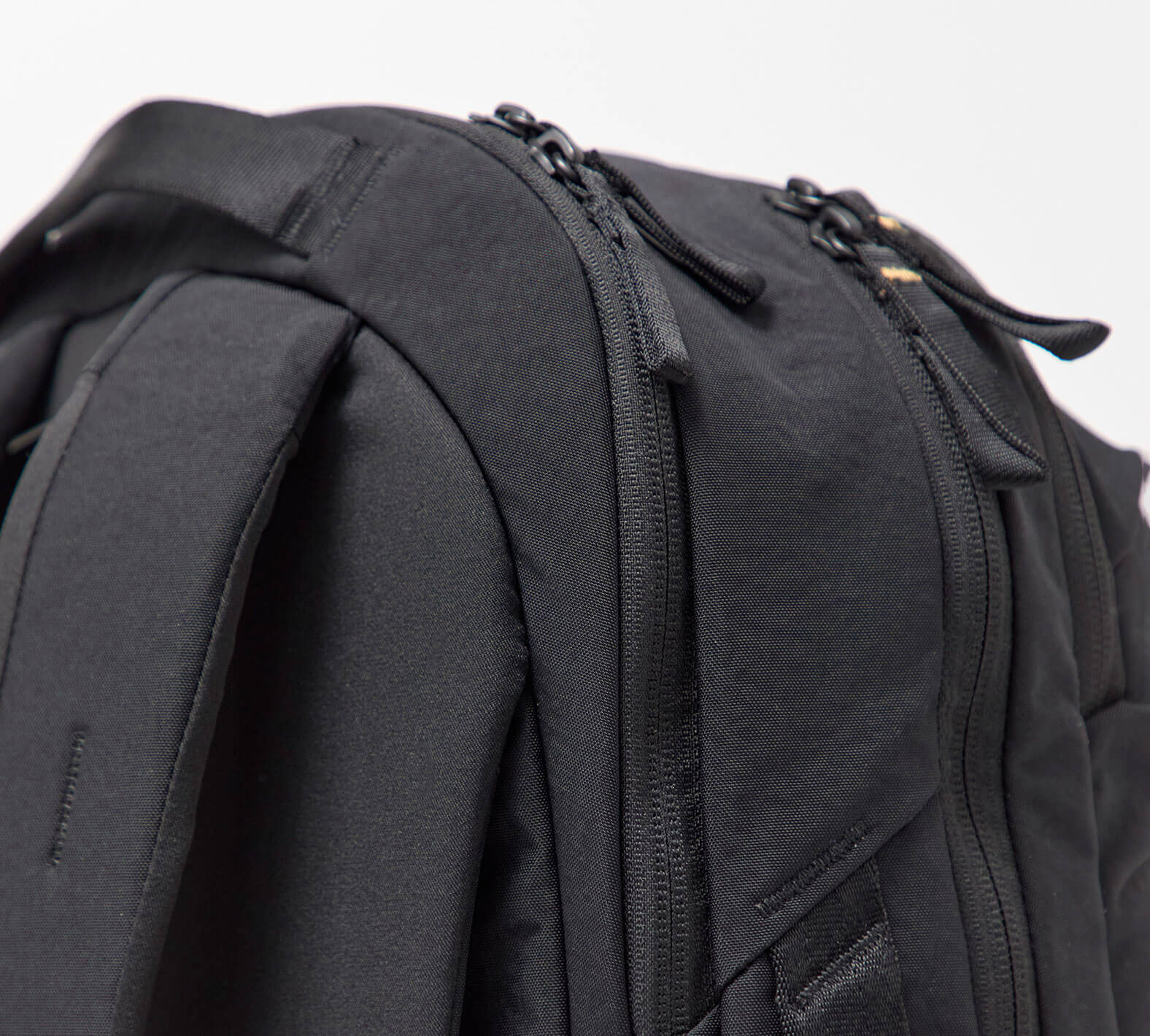 Close-up of a black backpack showing zippers, a padded shoulder strap, and fabric texture.