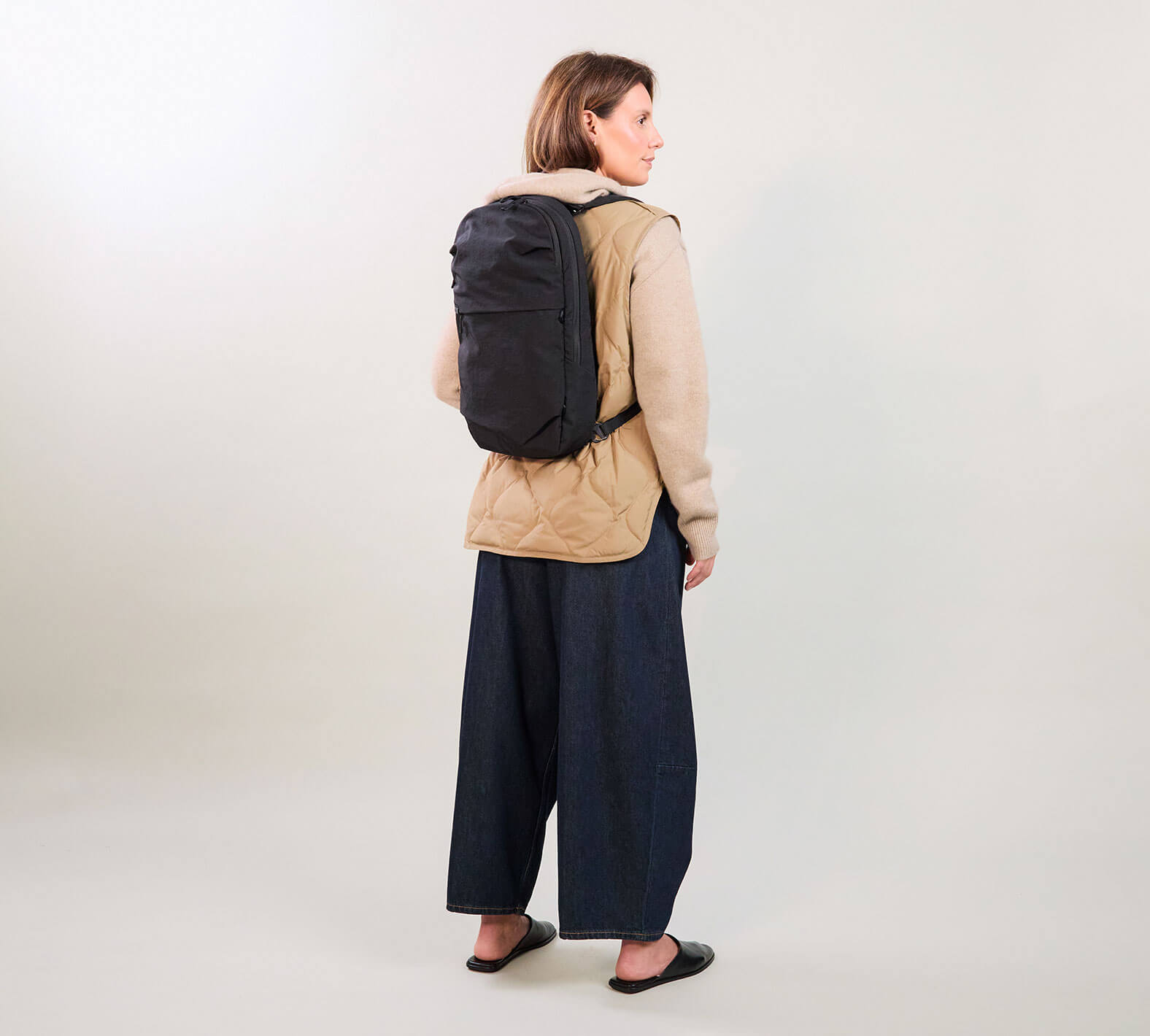 Back view of MODE Convertible Bag 14L in black worn as a backpack on a model, showing slim profile and top carry handle on a light studio background