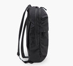 Black slim backpack, side view, padded shoulder straps, two zippered compartments and side pocket.